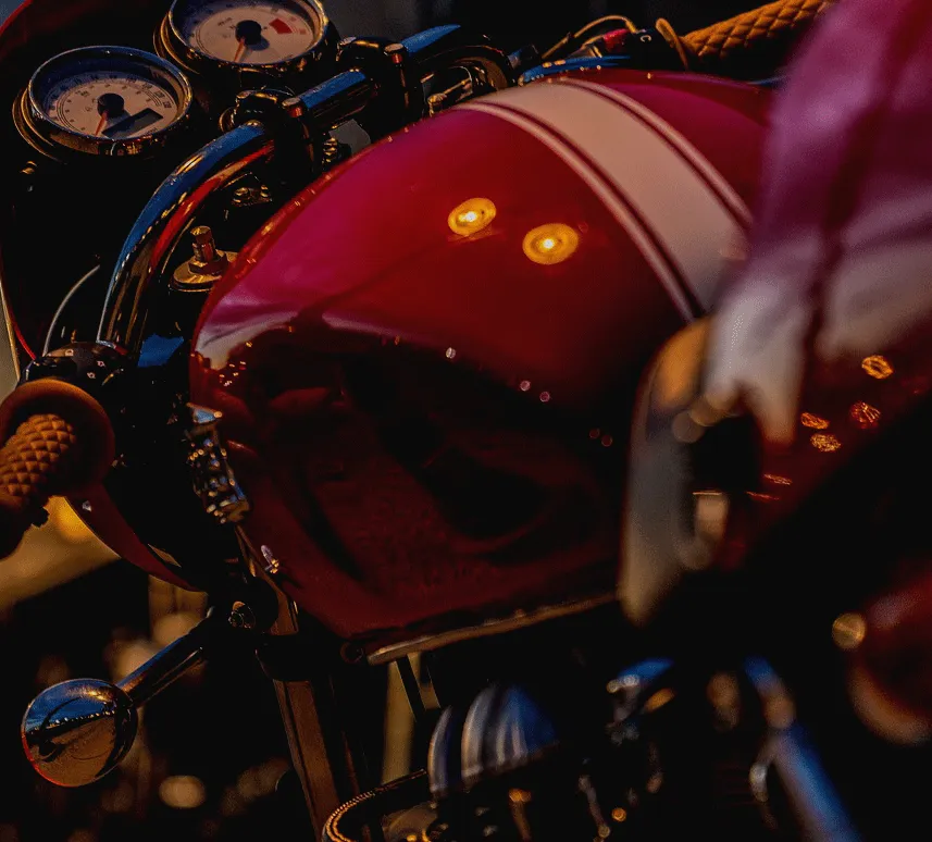 Close-up of a red Triumph fuel tank and twin clocks in evening light